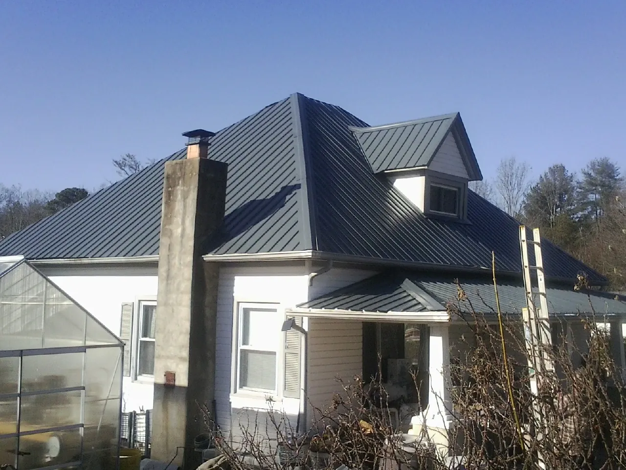 Dark blue standing seam metal roof on a white farmhouse with dormer — Slate & Tile Roof Repair by Roofing Brothers in Newnan