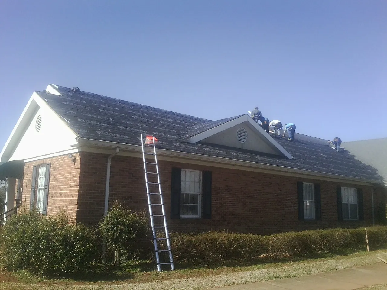 Crew tearing shingles off a brick ranch roof with a ladder set — Metal Roof Repair work by our crew in Newnan