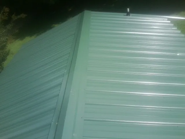 New green metal panels meeting at the ridge of a roof — Flat Roof Repair work by our crew in Newnan