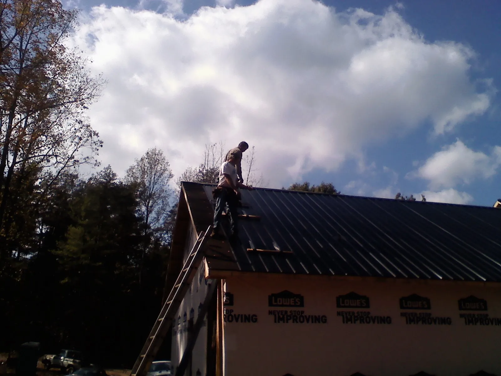 Roofer fastening dark metal panels high against a cloudy sky, from a Roof Inspection job in Newnan
