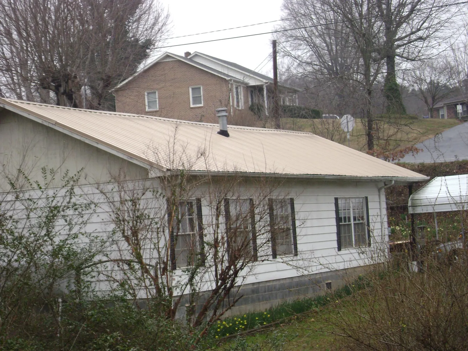 Tan metal roof on a white sided house set into a hillside — Commercial Roofing by Roofing Brothers in Newnan
