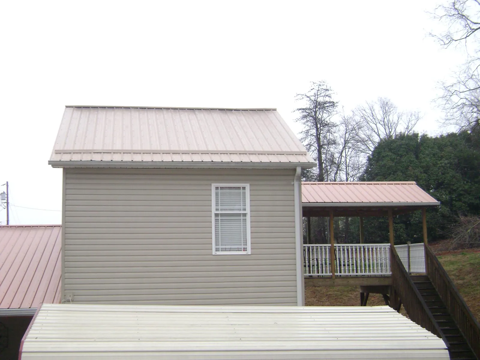 Tan metal roofs on a two story addition and attached porch, from a Roof Replacement job in Newnan
